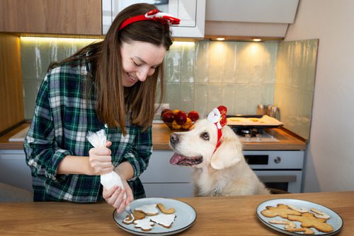 happy-woman-decorating-gingerbread-cookies-with-golden-retriever-dog-in-the-kitchen